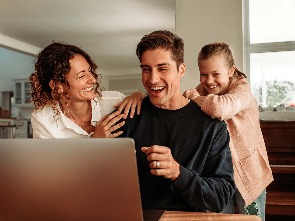 Padre, madre e hija se ríen frente al portátil en casa.