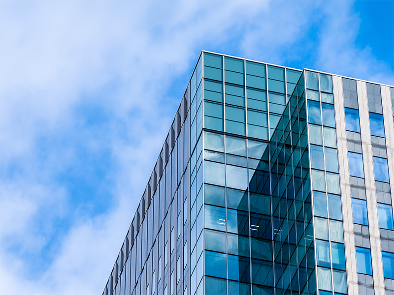Fachada de cristal de un edificio de oficinas bajo un cielo azul con nubes.
