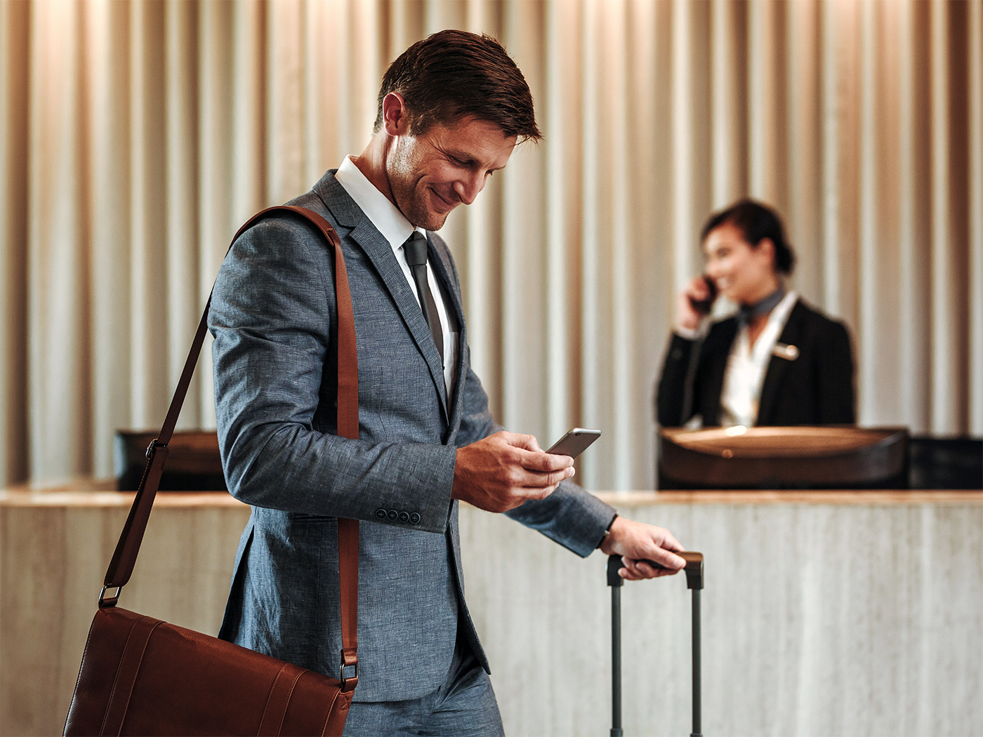 Ejecutivo con maleta revisa su celular en la recepción de un hotel.