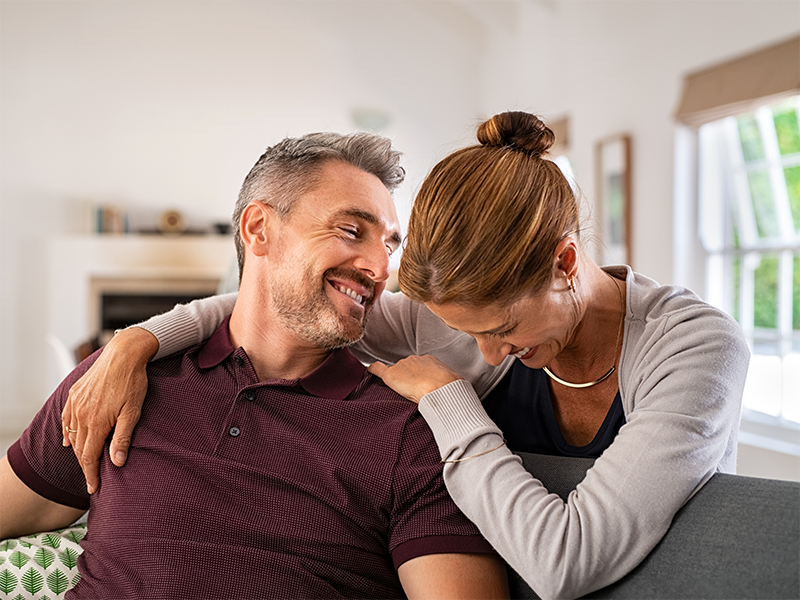  Hombre y mujer sonriendo abrazados en el sofá de una casa.
