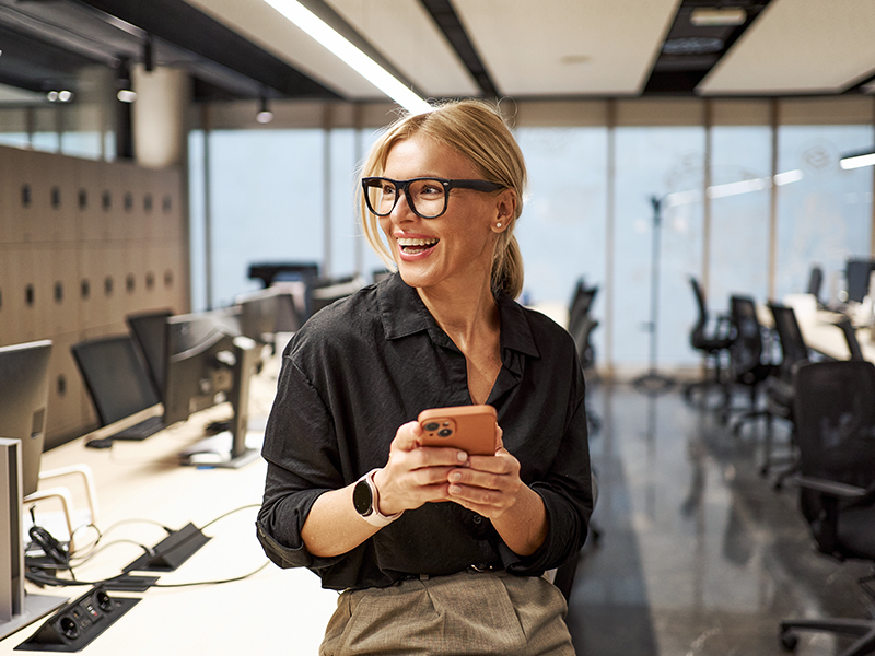  Mujer sonriente con gafas y teléfono en una oficina.