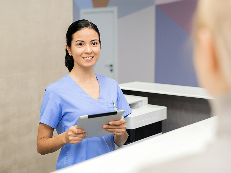 Profesional sanitaria atendiendo en el mostrador de recepción de una clínica.