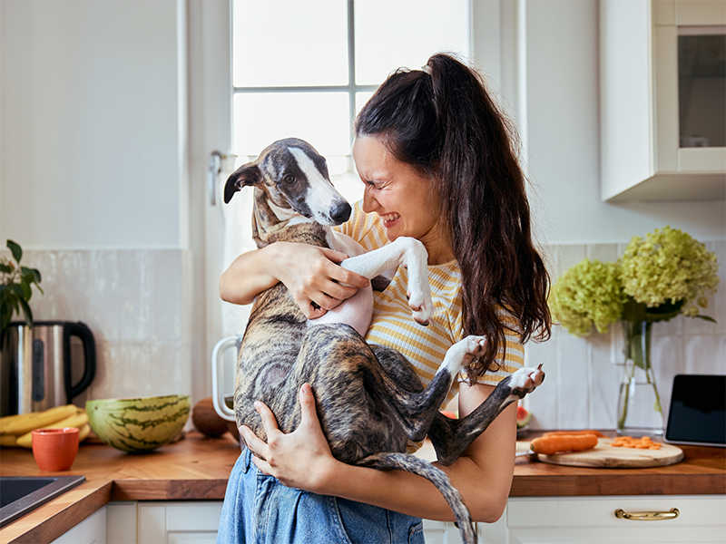 Mujer riendo con un perro en brazos en la cocina de casa