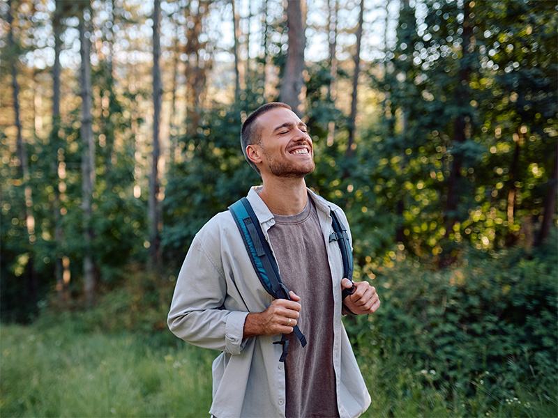 Persona sonriendo con los ojos cerrados en un bosque.