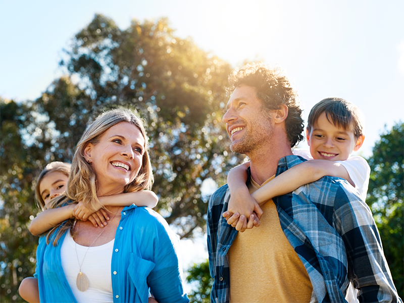 Familia sonriendo al aire libre con dos niños a cuestas