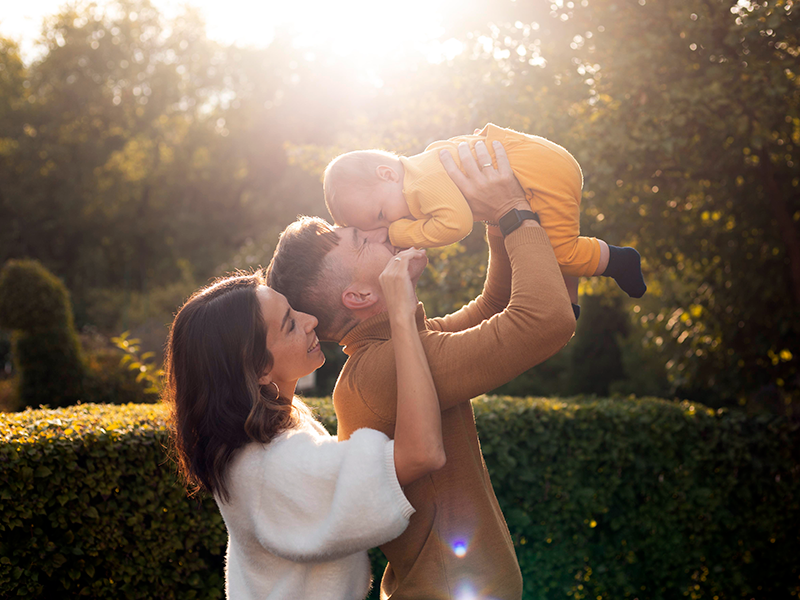 Padre y madre con su bebé en un jardín al atardecer.