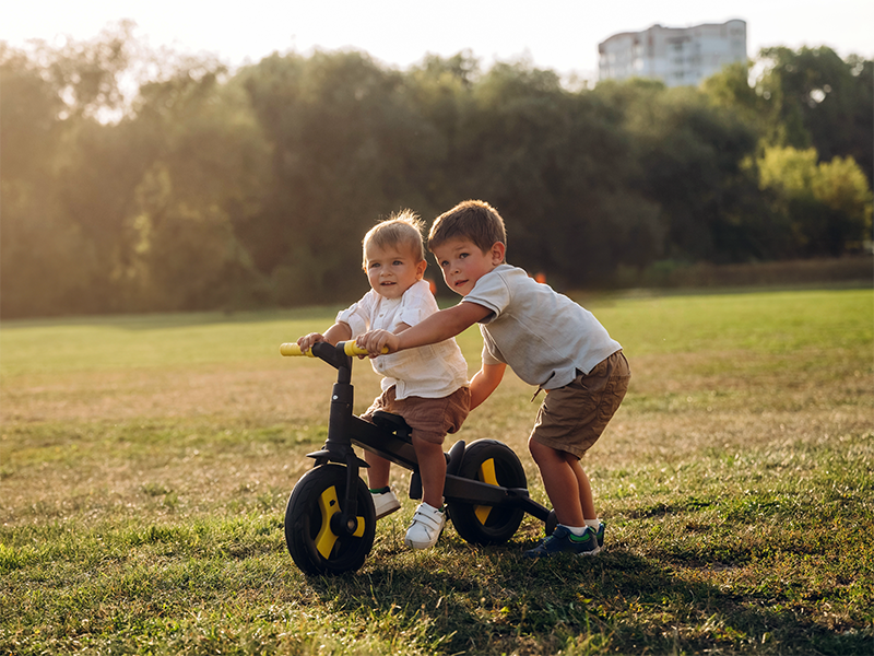 Dos hermanos juegan con una bici sin pedales en el parque.
