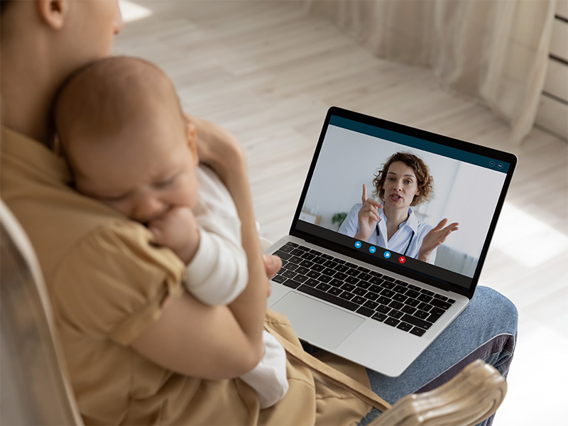 Madre con bebé en brazos en videollamada con una médica.