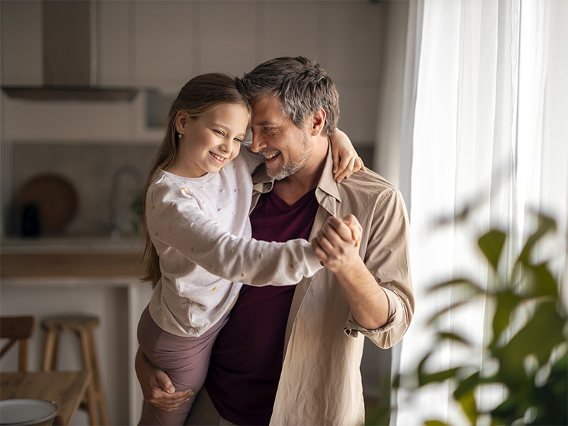 Hombre baila con una niña en brazos en la cocina.
