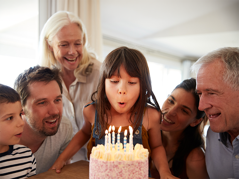 Niña soplando las velas de su tarta rodeada de su familia.