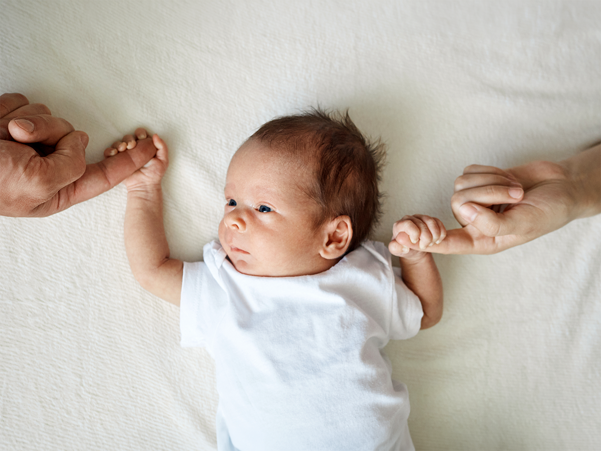Un recién nacido sujeta los dedos de sus padres sobre la cama.