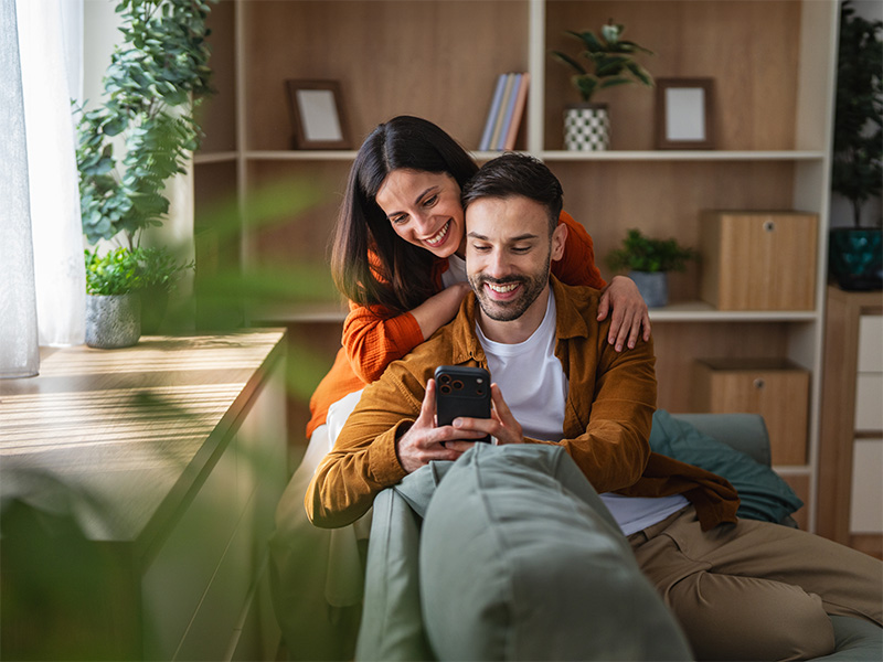 Pareja sentada en el sofa de su casa mirando el movil 