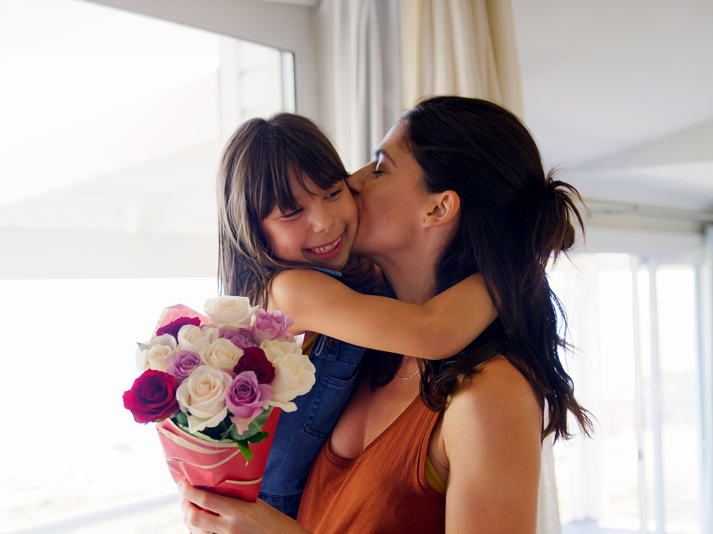 Madre e hija se abrazan con un ramo de flores.